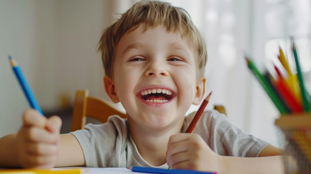 Portrait of a smiling little boy drawing with pencils at homeの素材
