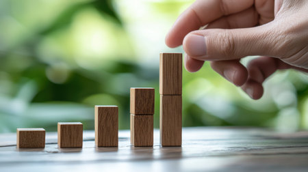 A hand is placing wooden blocks on top of each other, creating a stack. The blocks are arranged in a way that they resemble a graph or a chart, with each block representing a different level or stepの素材