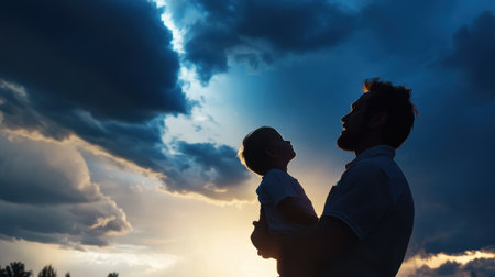 A man holds a child in his arms while looking up at the sky. The sky is cloudy and the sun is setting, creating a moody atmosphere. The man and child seem to be enjoying the moment togetherの素材