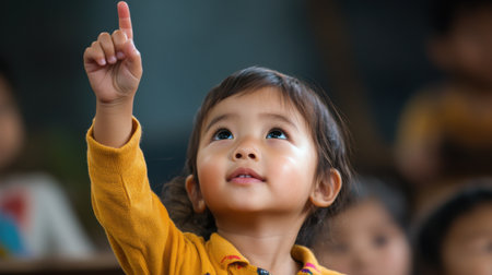 A young girl is pointing up with her finger. She is smiling and she is happy. The other children in the room are watching herの素材
