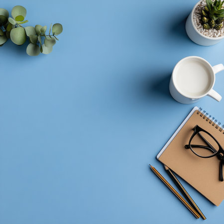 A blue background with a white cup and a plant. A notebook and a pair of glasses are on the tableの素材
