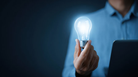 A person holding a light bulb in their hand. The light bulb is glowing brightly, and the person is wearing a blue shirt. Concept of innovation and creativityの素材