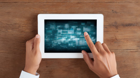 A person is pointing at a tablet with a blue screen. The tablet is on a wooden tableの素材