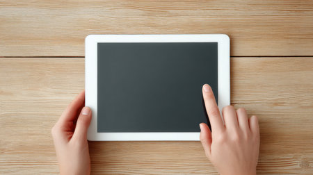 A person is holding a tablet with a black screen. The tablet is on a wooden tableの素材