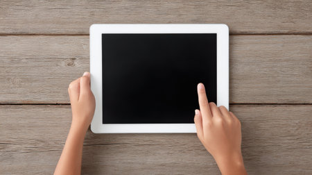 A child is pointing at a tablet on a wooden table. The tablet is black and white, and the child is holding it in their hand. Concept of curiosity and explorationの素材