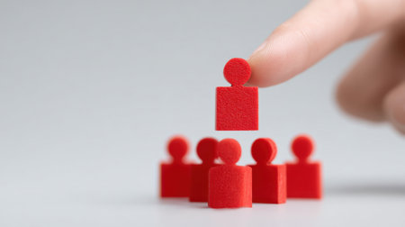 A hand is holding up a red block with a person on it, and there are five other red blocks in a row. Concept of leadership and hierarchy, with the person on the block being the leaderの素材