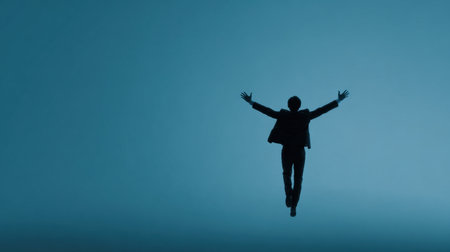 A man is jumping in the air with his arms outstretched. The sky is blue and the man is the only person in the image. Scene is uplifting and inspiringの素材