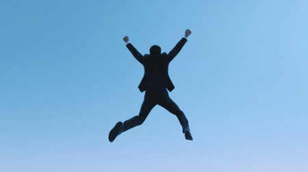 A man in a suit is jumping in the air with his arms raised. Concept of triumph and accomplishmentの素材