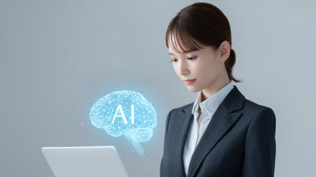 A woman is sitting in front of a laptop with a brain image on the screen. The image is blue and has the word AI written on it. The woman is focused on her workの素材