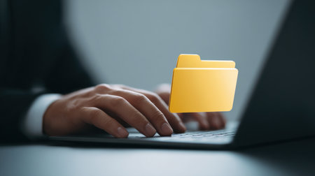 A man is typing on a laptop with a yellow folder on the screen. The folder is open and the man is using the keyboard to type. Concept of productivity and focusの素材