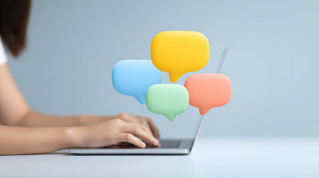A woman is typing on a laptop with a colorful chat bubble on the screen. The chat bubble is made up of different colored shapes, and it is a message or a conversationの素材