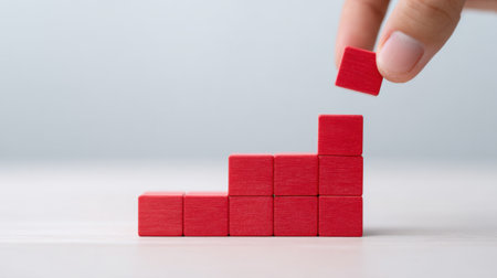 A person is holding a red block and breaking it into pieces. Concept of progress and growth, as the blocks are stacked on top of each other, and the person is taking a piece awayの素材
