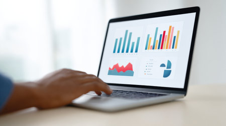 A laptop screen shows a person typing on a keyboard. The laptop is open to a graph that displays various data points. The person appears to be working on a project or analyzing the data on the screenの素材