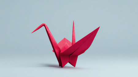 A red origami bird is sitting on a grey background. The bird is made of paper and has a unique design. Concept of creativity and artistry, as well as a sense of calmness and tranquilityの素材