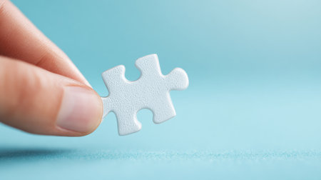 A hand holding a white puzzle piece on a blue background. Concept of curiosity and the idea of solving a puzzleの素材
