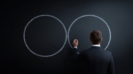 A man is drawing two circles on a blackboard. The circles are connected by a line, and the man is wearing a suit. Concept of professionalism and focusの素材