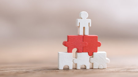 A man is standing on top of a stack of puzzle pieces. The puzzle pieces are red and white. Concept of teamwork and collaboration, as the man is the only one standing on top of the puzzle piecesの素材