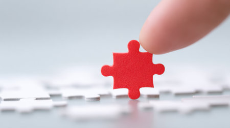A hand is reaching for a red puzzle piece on a white puzzle. The puzzle piece is missing, and the hand is trying to find itの素材