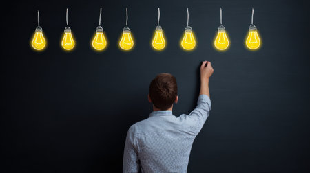 A man is drawing a line of light bulbs on a blackboard. Concept of creativity and innovation, as the light bulbs represent new ideasの素材