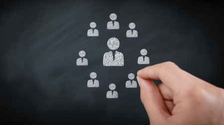 A hand is drawing a group of people on a chalkboard. The people are all dressed in business attire and are standing in a circle. Concept of teamwork and collaborationの素材
