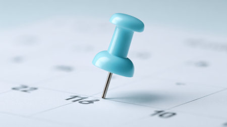 A blue pin is placed on a calendar with the number 16 on it. The pin is pointing to the number 16, indicating that it is an important date or event. The pin is small and brightの素材