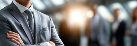 A man in a suit is standing in front of a group of people. He is wearing a tie and has his arms crossed. Concept of professionalism and formality, as the man is dressed in a suit and tieの素材
