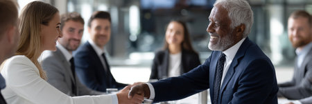 A man shakes hands with a woman in a business meeting. The man is wearing a suit and tieの素材