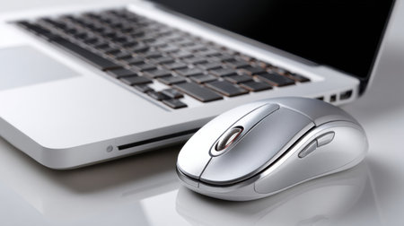 A silver computer mouse sits on a white laptop. The mouse is positioned on the right side of the laptop, and it is the primary focus of the image. The laptop is openの素材