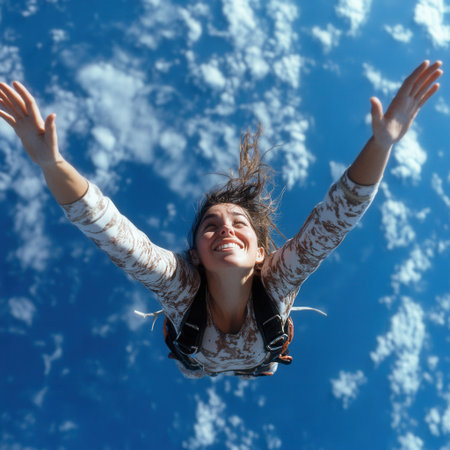 A woman is flying through the air with her arms outstretched. The sky is blue and there are clouds in the background. The woman is happy and free as she soars through the airの素材