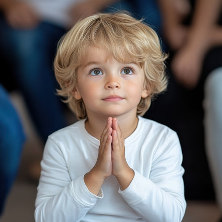 A young blonde boy is praying with his hands together. He is wearing a white shirt and has a serious expression on his faceの素材