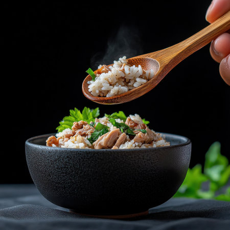 A person is holding a spoon and scooping food from a black bowl. The bowl contains rice and meat, and the spoon is filled with rice. Concept of comfort and warmth, as the person is enjoying a mealの素材