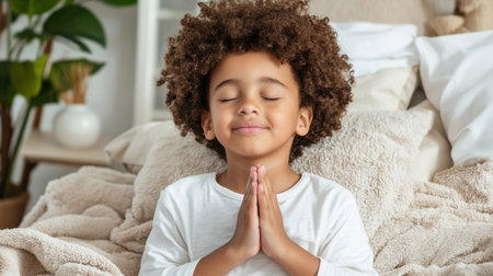 A young child is praying in bed. The child is smiling and he is in a peaceful and calm stateの素材