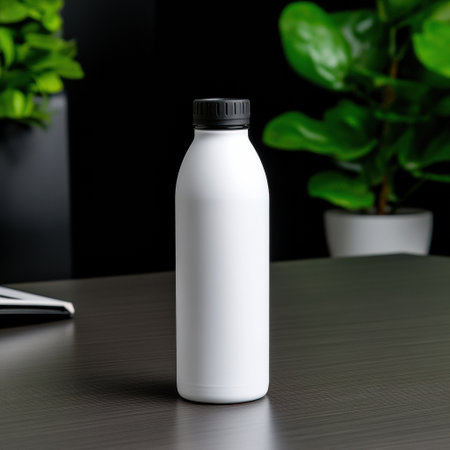 A white bottle sits on a table next to a potted plant. The bottle is tall and slender, with a black cap. The table is made of wood and has a dark surfaceの素材