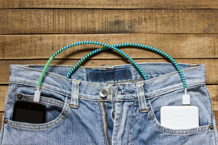 power bank lies in a back pocket of jeans, in the other is a mobile phone that is charged.の写真素材