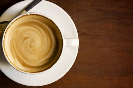 White cup of cappuccino with latte art on wooden background at coffee cafe.の写真素材