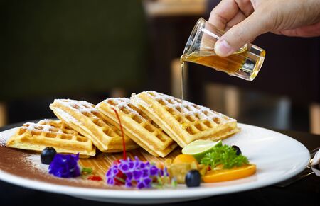 Honey pouring on a fresh waffles on a plate. Breakfast with waffles in morning.