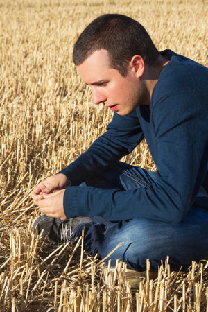 Reflecting Young Sitting on a grain field in summer harvestのeditorial素材