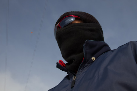 Man totally covered with sunglasses and balaclava with sky background and power line 