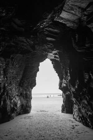  View in black and white from inside a cave on the beach of the Cathedrals with overseas visitors in Spainの写真素材