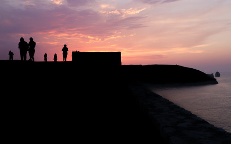 Silhouettes of people silhouetted against a sky enjoying a beautiful sunset, a walk along the sea coast of Llanes Asturiasの写真素材