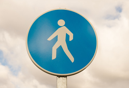 Traffic signal circular blue isolated on white background of cloudy sky. Mandatory route for pedestriansの写真素材