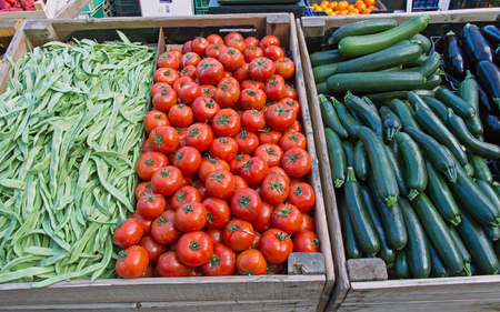 Wooden boxes with vegetables in a market exposed outdoors (tomatoes, zucchini, eggplant, beans, pods)の写真素材