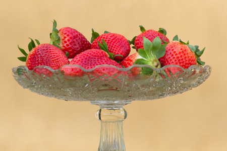 Glass bowl container containing fresh fruit bowl and fresh strawberries on uniform background of ocherの写真素材