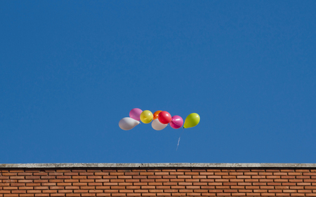 Colorful balloons flying through the air, above the top of a buildingの写真素材