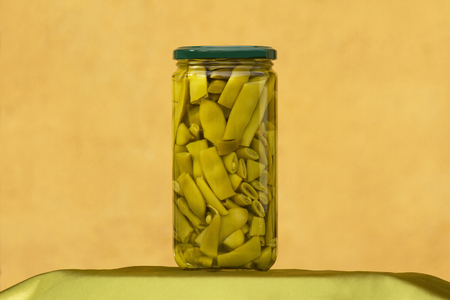 Jar or glass container showing green canned beans with ocher wall backgroundの写真素材