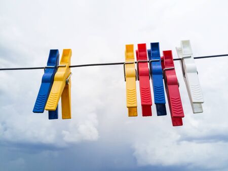 Colored clothespins holding clothesline to dry, with cloudy sky backgroundの写真素材