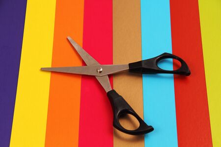 Steel scissors with black handles lying on colorful cardboard, lined with bars の写真素材