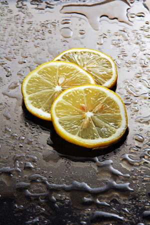 ut into round slices of lemon on dark glass with water drops の写真素材