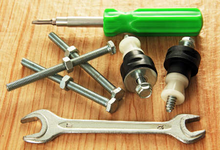 bolts, nuts, screw fastening, a wrench and a screwdriver on a wooden table 