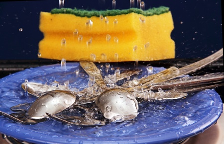 fork, spoon and table knife on blue plate under running water 